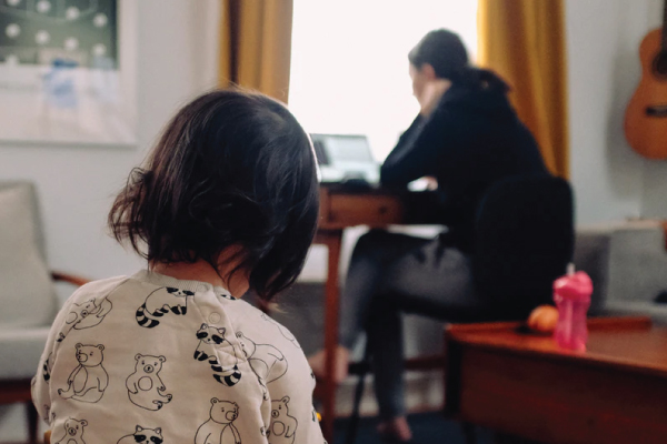 little girl sitting on couch watching her mother working on from home on her laptop from her desk